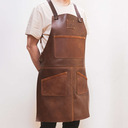 A carpenter wearing a white t-shirt stands with his hands on his hips, donning a well-made brown leather toolbelt from The Durham Leatherworker with multiple pockets, against a plain background.