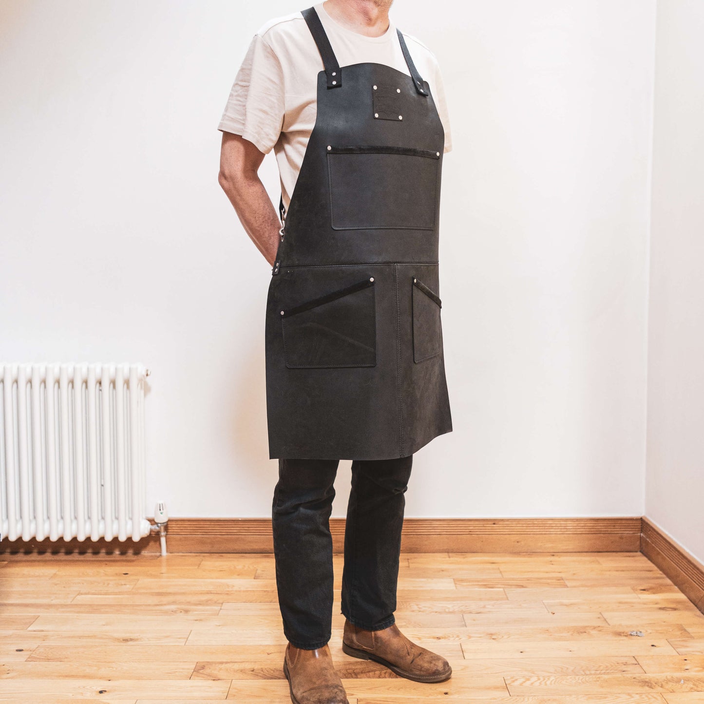 A joiner wearing a dark apron by The Durham Leatherworker stands in a room with wooden flooring, partially facing the camera but not showing their face.