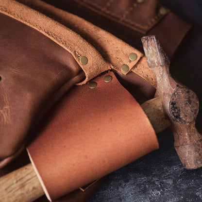 Close-up of a Belt Bag 1 from The Durham Leatherworker and a hammer on a textured surface, highlighting the rustic texture of the leather and the worn handle of the hammer.