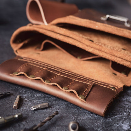 Close-up of an open brown leather Belt Bag 1 tool roll with empty slots and scattered metal tool bits on a textured dark surface, ideal for a woodwork joiner by The Durham Leatherworker.